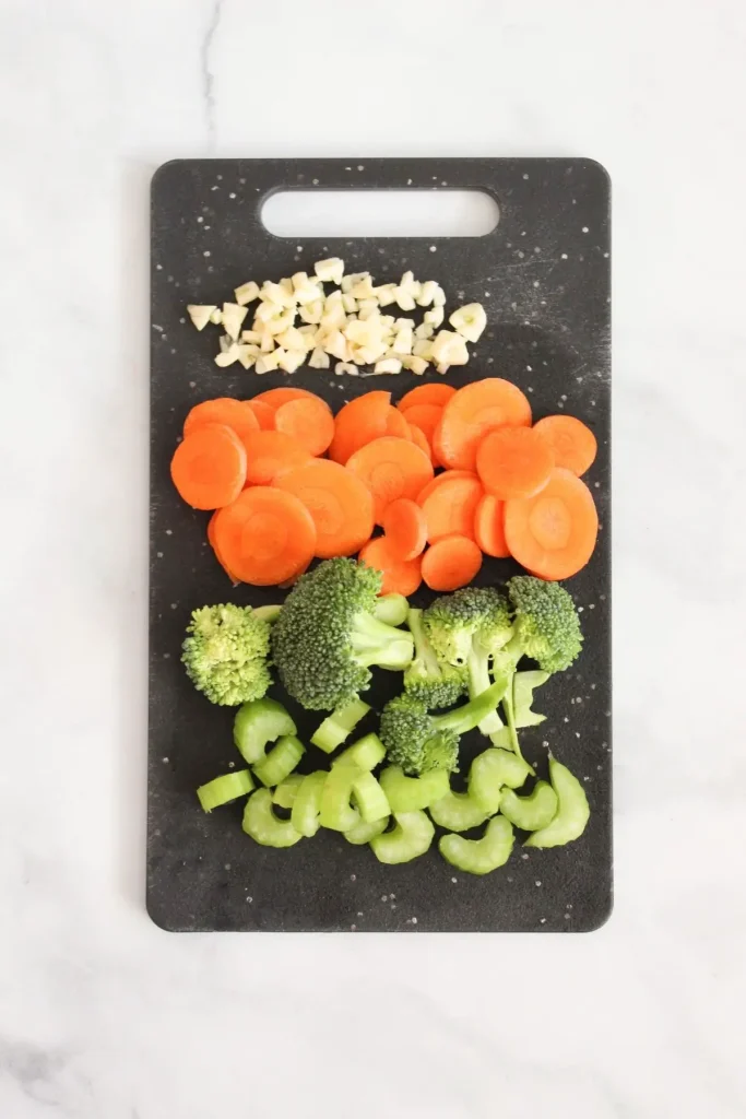 chopped up garlic, carrots, broccoli, and celery on black cutting board