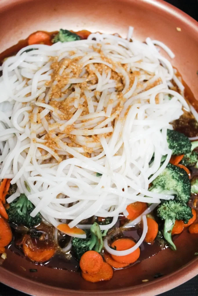 adding pad thai sauce to rice noodles and sauteed veggies 