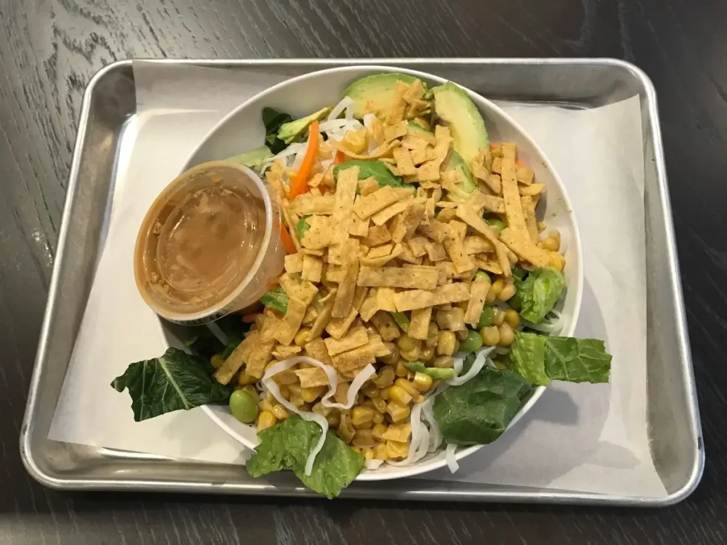 create your own salad from corelife eatery with lettuce, tortilla strips, rice noodles, corn, edamame, carrots, and dressing on a silver tray