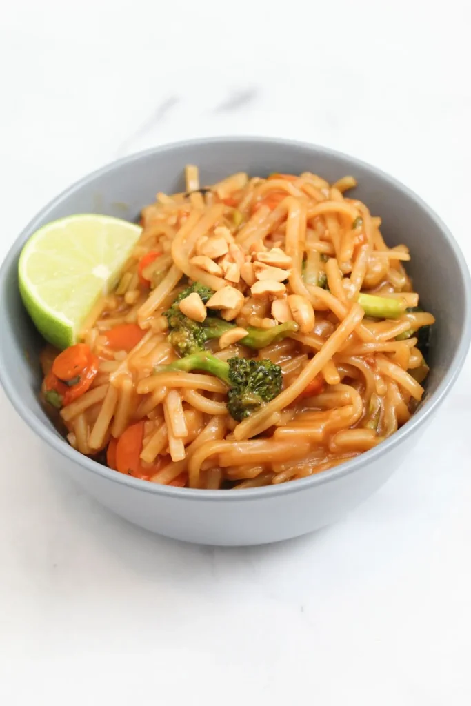 finished pad thai meal topped with chopped peanuts lime