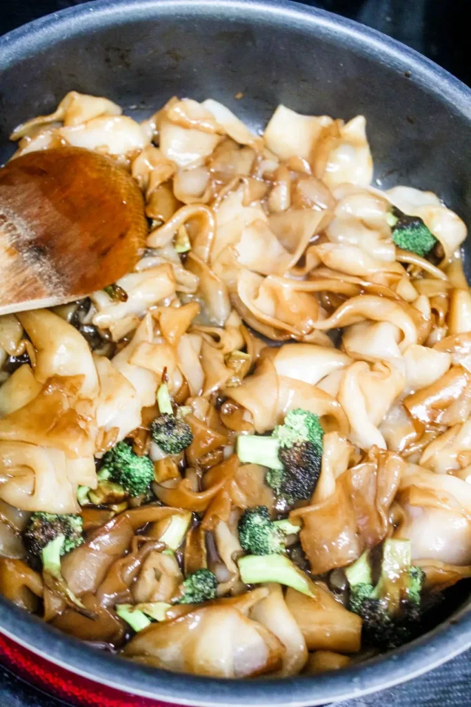 mixing the pad see ew sauce with broccoli and noodles