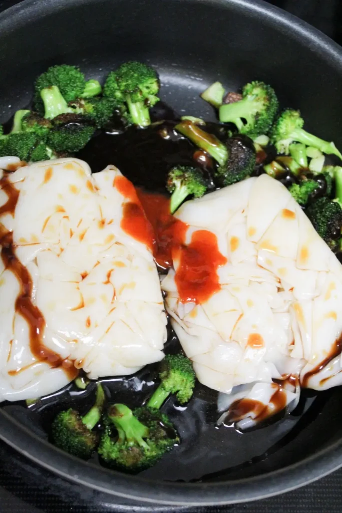 putting pad see ew noodles into the pan with the sautéed broccoli and sauce