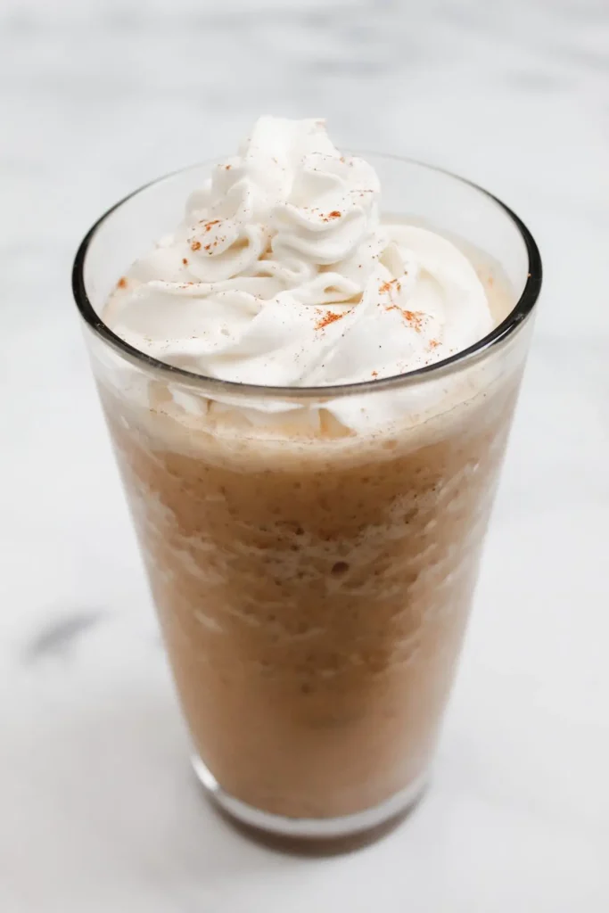 vegan pumpkin spice cream frappuccino with dairy free whipped cream in a glass with a white background