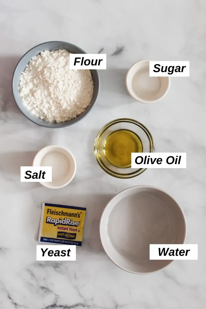 Individual ingredients for vegan pizza dough in small bowls including yeast, water, flour, sugar, salt, and olive oil