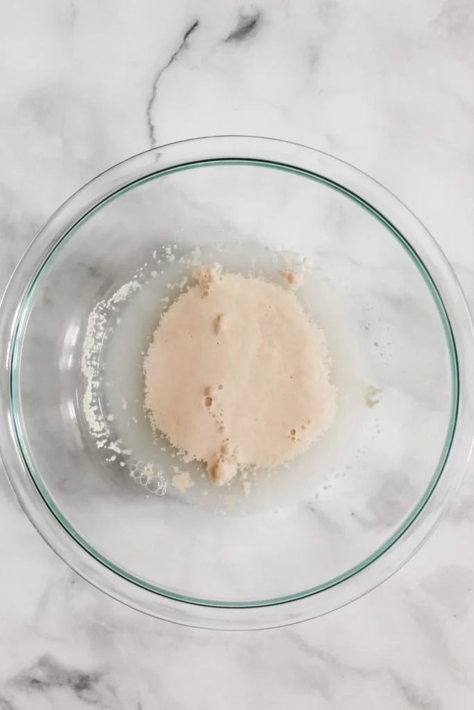 making pizza dough by mixing yeast, sugar, and warm water together in large glass bowl