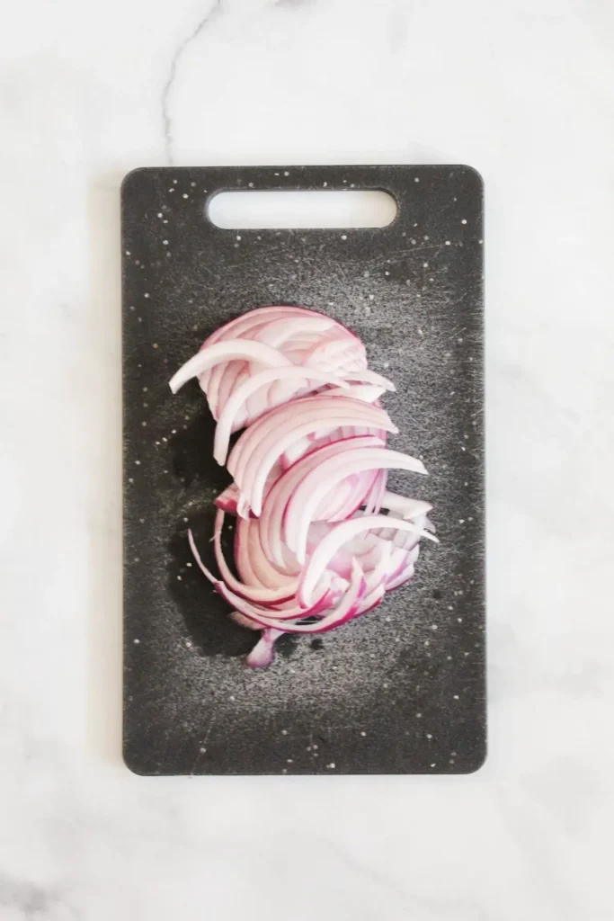 red onions cut into strips on black cutting board