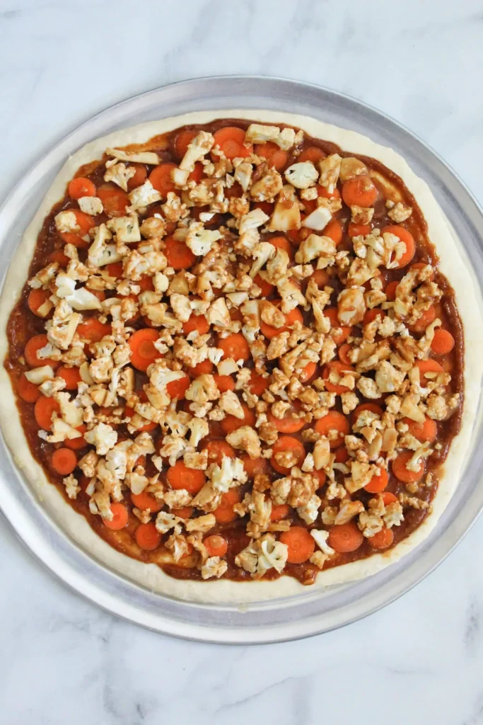 thai pizza topped with sauce, cauliflower, and carrots ready to go in the oven