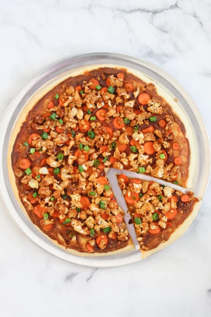 top down view of finished vegan thai pizza with slice cut out on pizza pan