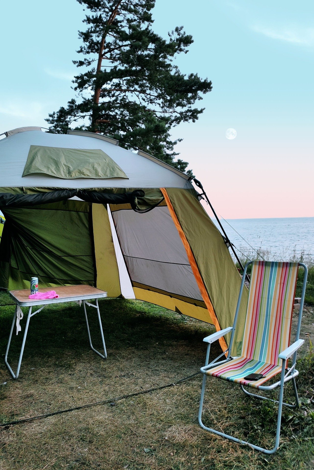 a tent with a chair and table, next to the water.